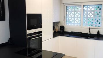 A modern kitchen with white cabinets, a black countertop, a built-in oven, and a microwave.