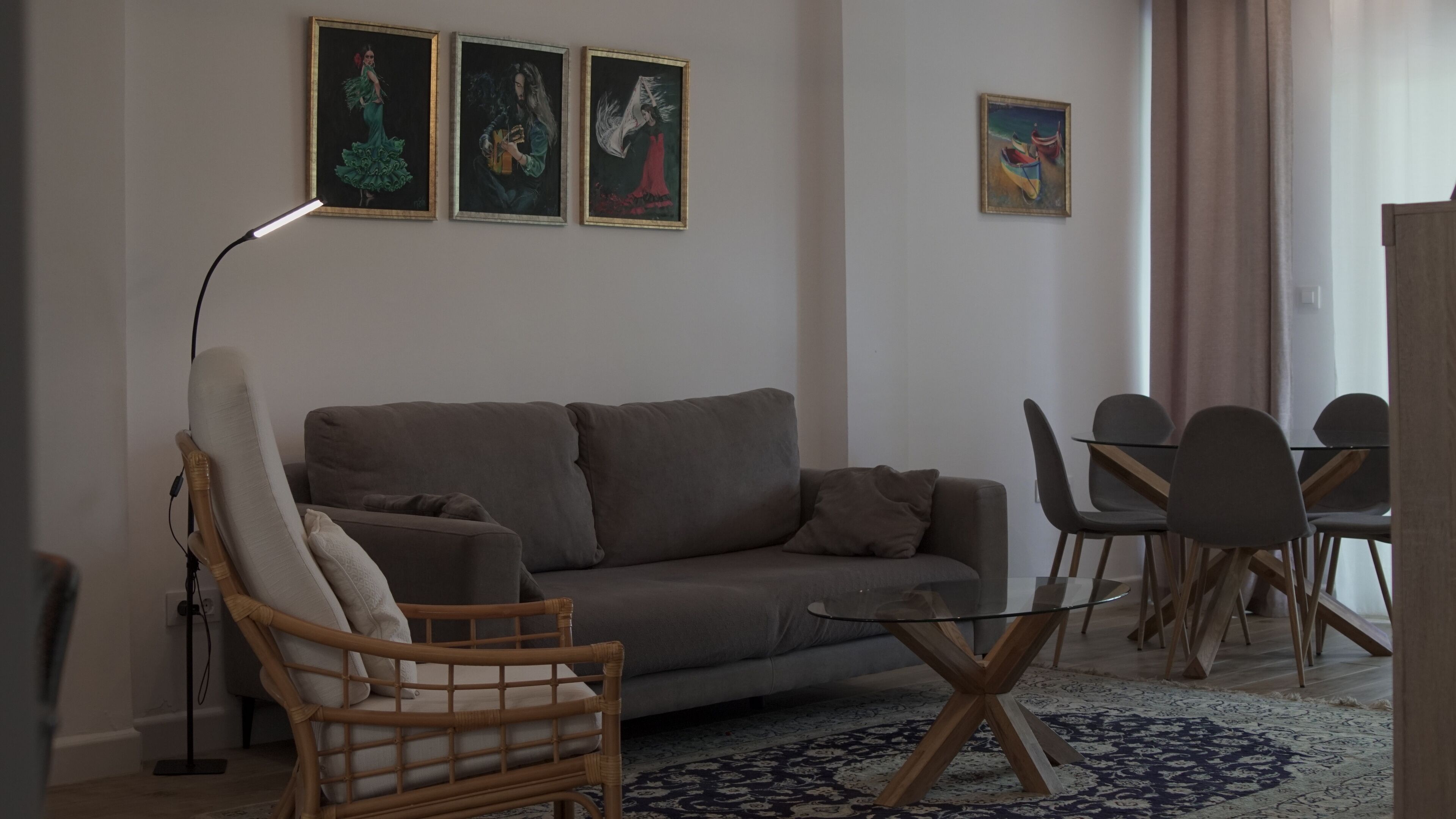 En stue med sofa, stol, sofabord i glas og et spisebord med stole. Tre billeder hænger på væggen.
