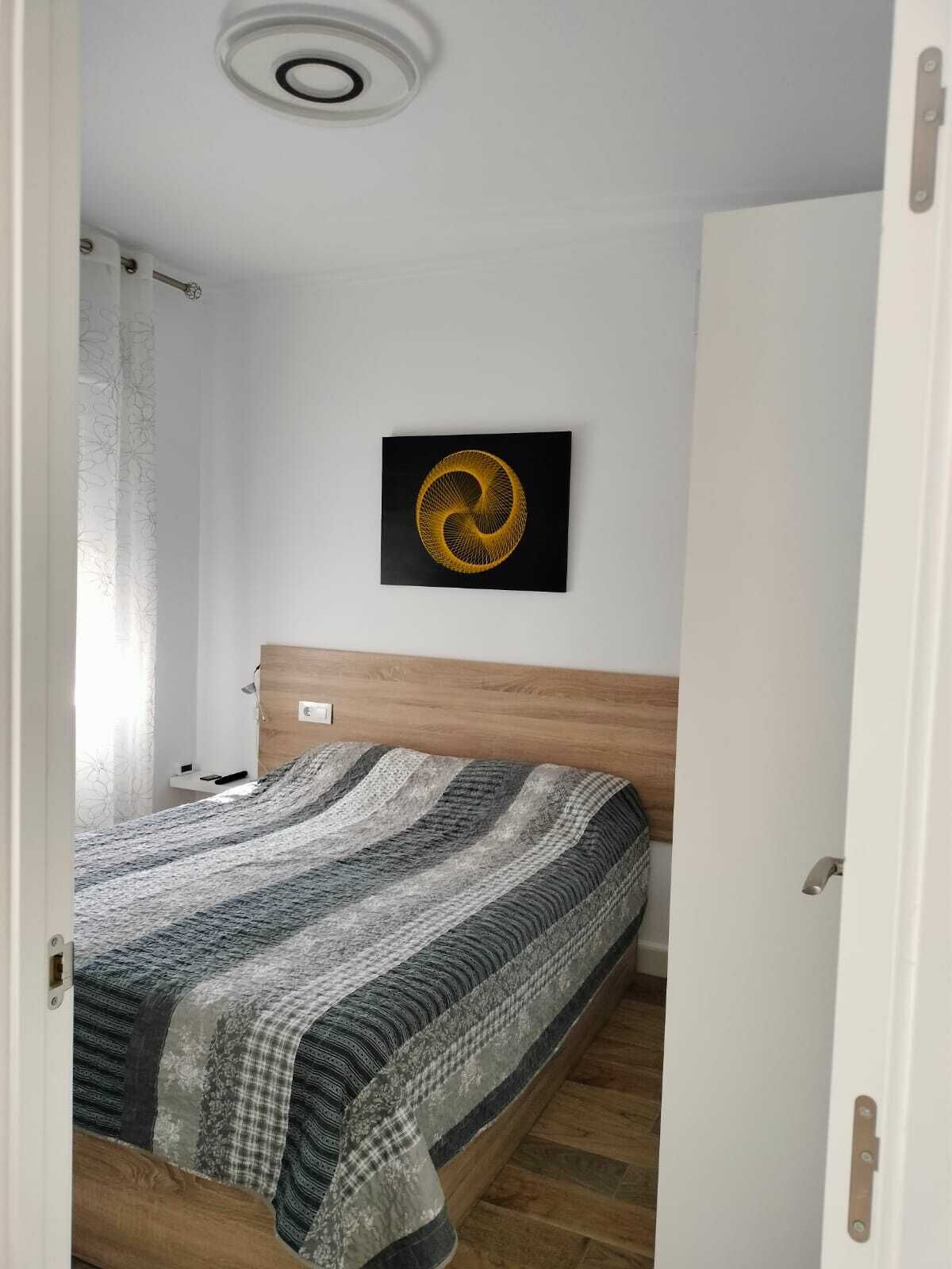 A bedroom with a bed, a headboard, a wall-mounted artwork, and a ceiling light fixture.