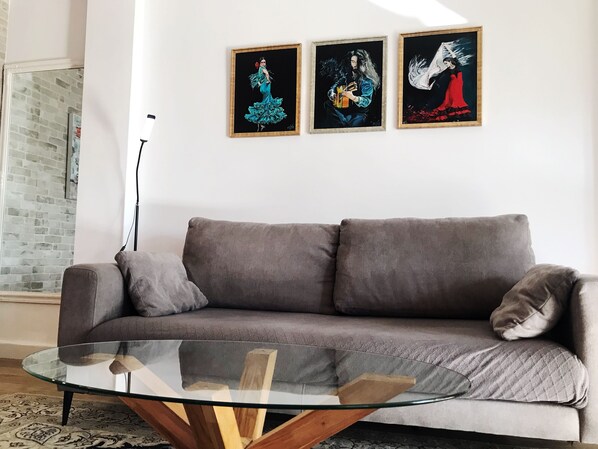 A modern living room with a grey sofa, a glass coffee table, and three framed artworks on the wall.