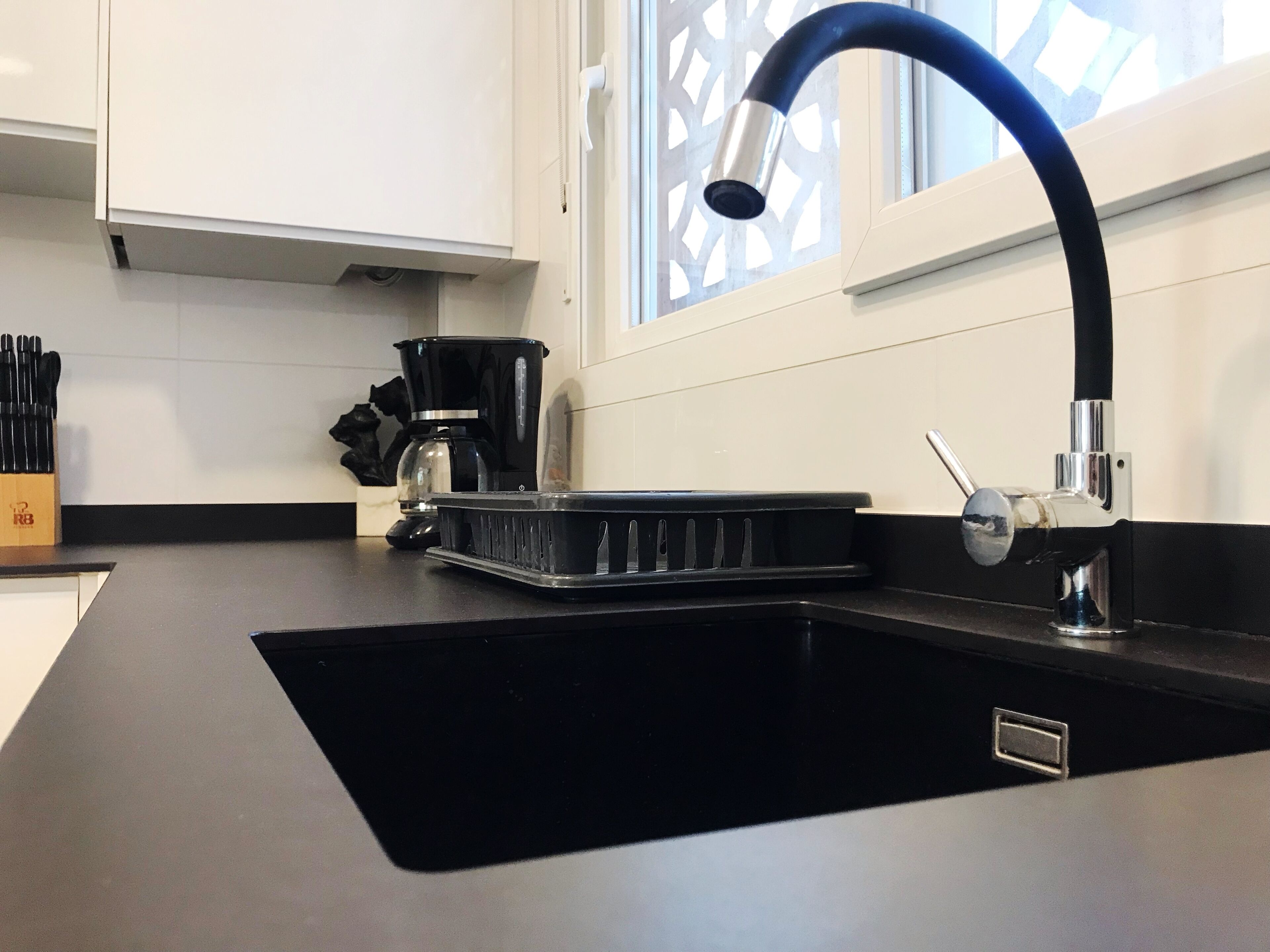 Een moderne keuken met een zwart spoelbak, een koffiezetapparaat en een raam met decoratief spijlenwerk.