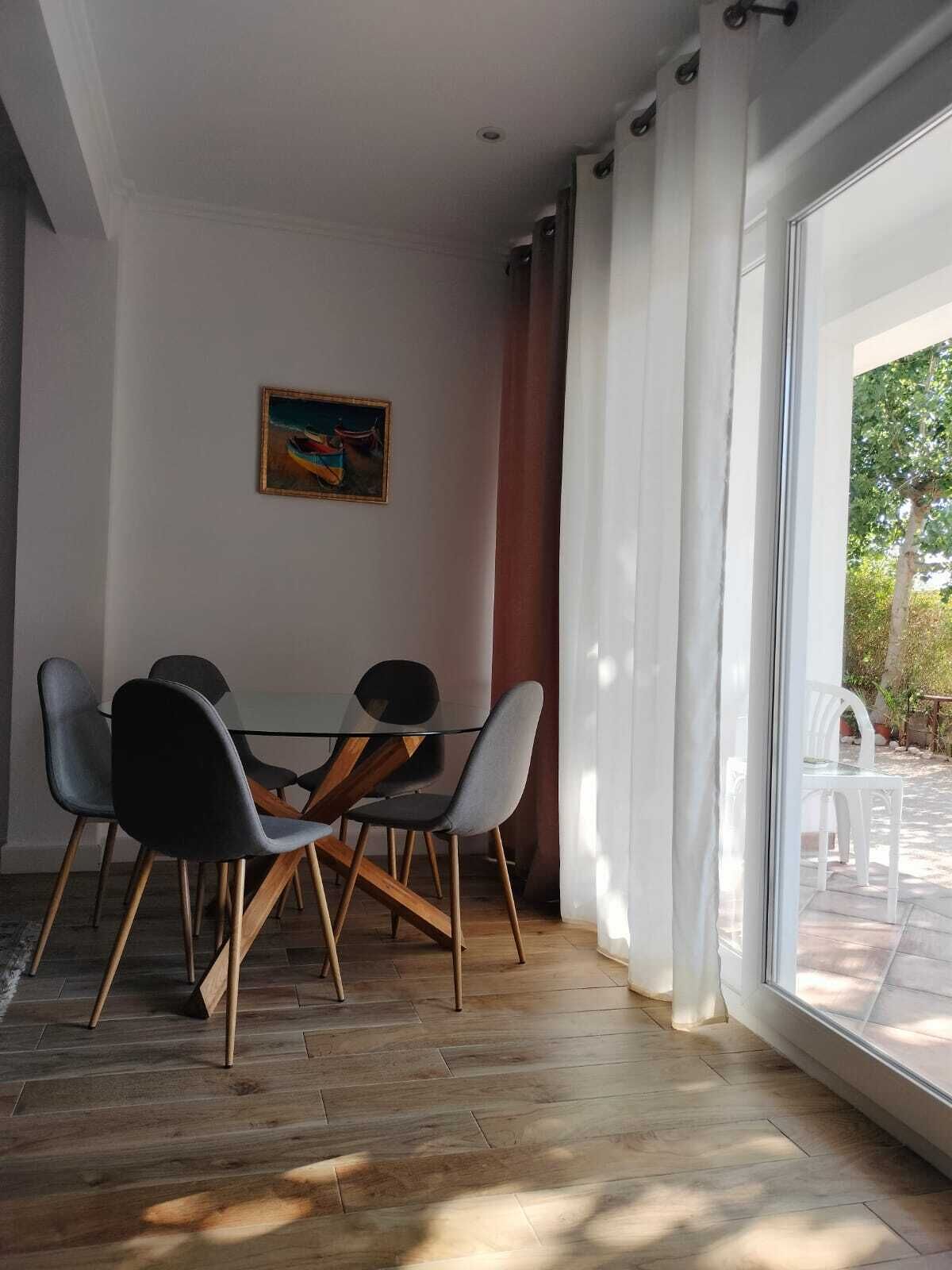 Un comedor con una mesa y sillas de vidrio, un cuadro en la pared y vistas al exterior a través de amplios ventanales.
