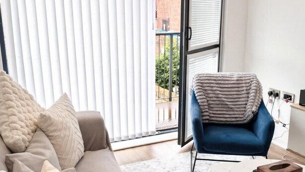 Ett modernt vardagsrum med en soffa, en blå fåtölj, ett soffbord och utsikt genom ett stort fönster.