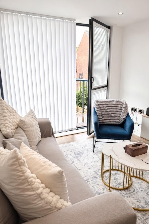 A modern living room with a sofa, a blue armchair, a coffee table, and a view through a large window.