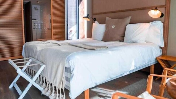 Une chambre moderne avec un grand lit, une tête de lit en bois et un petit coin salon comprenant une chaise et une table.