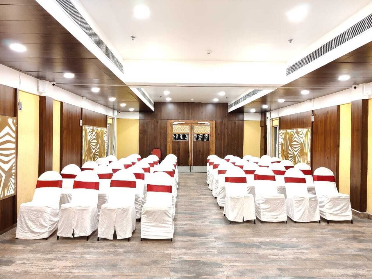 A conference room with rows of white chairs with red sashes, wooden paneling, and a large door at the front.