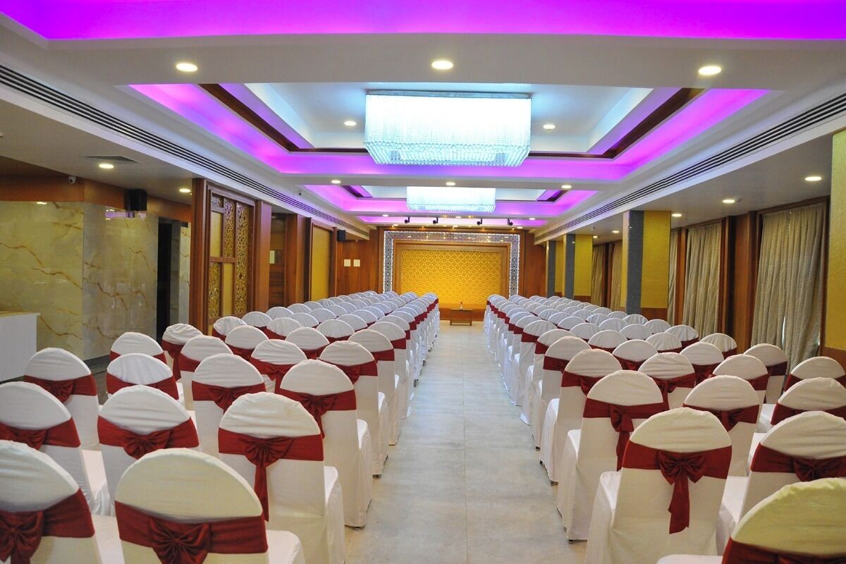 A conference room with rows of chairs, each with a white cover and red sashes, and a stage at the front.