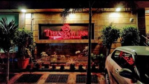 L’entrée d’un hôtel, avec une enseigne au néon indiquant : « THANMAI INN ».