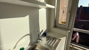 Eine moderne Küche mit Spüle aus Edelstahl, weißen Schränken und einem Fenster mit Blick auf ein Backsteingebäude.