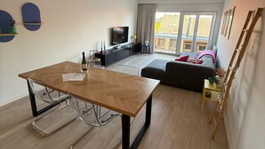 Ein modernes Wohnzimmer mit Essbereich, einer Couch, einem Fernseher und einem Balkon mit Blick.
