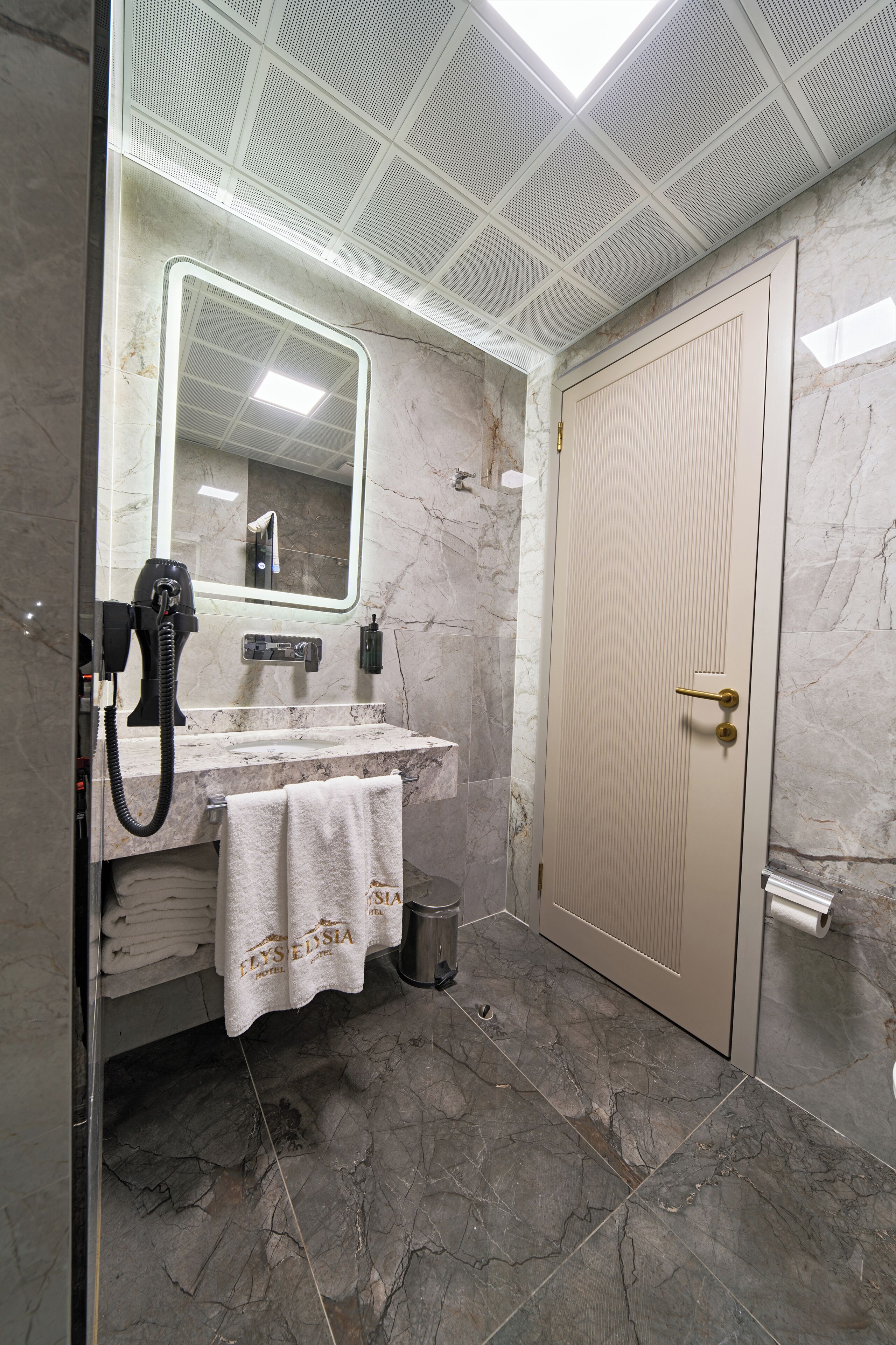 A bathroom with a marble floor, a sink with a towel, a mirror, and a door.