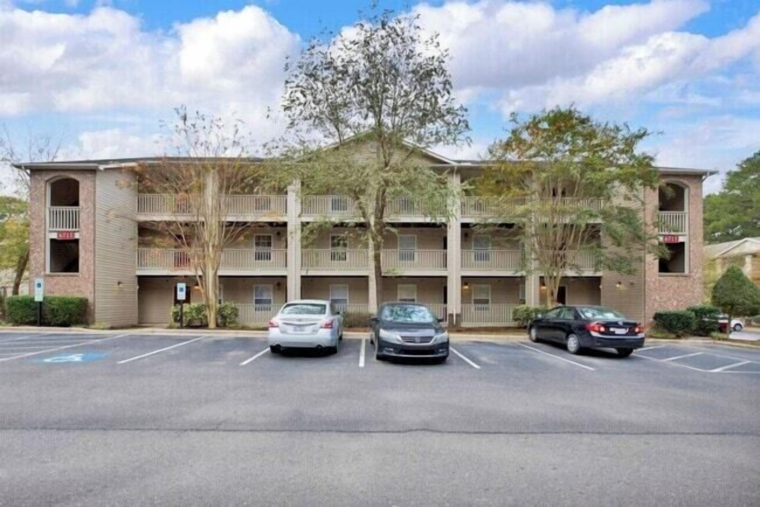 Un hotel de varios pisos con un atrio central, plazas de estacionamiento y un árbol en la parte delantera.