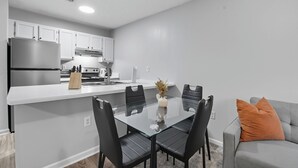 A modern kitchen with white cabinets, a stainless steel refrigerator, and a glass dining table with black chairs.