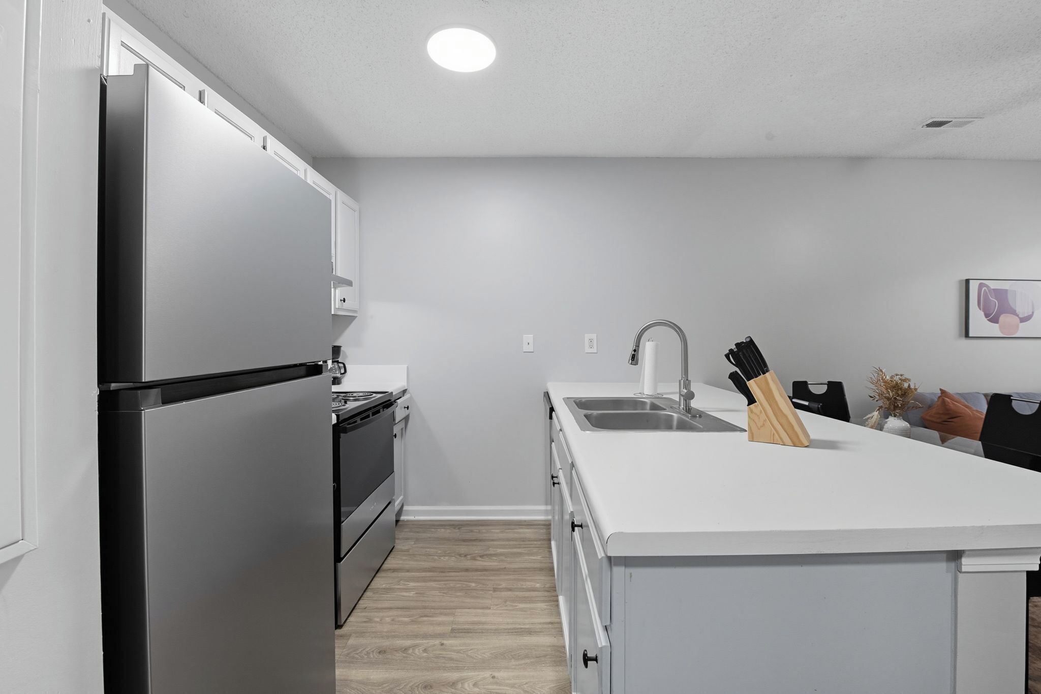 Una cocina moderna con un refrigerador de acero inoxidable, horno empotrado y encimera blanca.