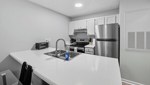 A modern kitchen with white cabinets, stainless steel appliances, and a white countertop. - Cozy Contemporary Stay I Pool & Gym I Free Parking (Fayetteville)