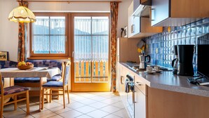 Une cuisine avec un coin repas, une fenêtre avec des rideaux et une machine à café posée sur le plan de travail.