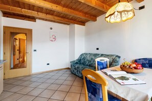 A room with a wooden ceiling, a sofa, a dining table with a bowl of fruit, and a magazine.