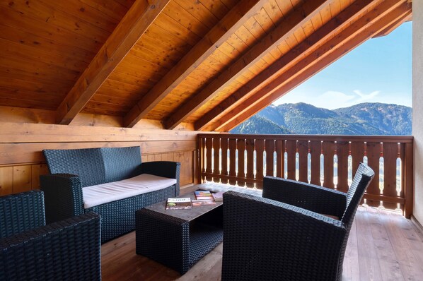 A wooden balcony with wicker furniture, a wooden ceiling, and a view of mountains.