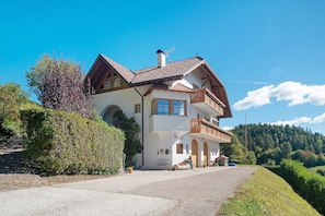 A two-story house with a balcony, a chimney, and a driveway leading to the entrance.