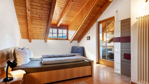 Une chambre à coucher aménagée dans un espace de type « loft », avec un plafond en bois, un lit avec des oreillers, un bureau avec une lampe et une fenêtre.
