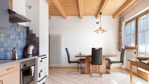 Keittiössä on liesi, uuni ja pesuallas, ruokapöytä tuoleineen sekä ikkuna, jossa on verhot.