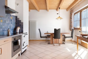 A kitchen with a stove, oven, and sink, a dining table with chairs, and a window with curtains.