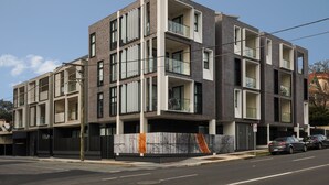 A modern multi-story building with a mix of brick and glass facade, balconies, and a gated entrance.