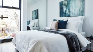 A modern bedroom with a large bed, a window, and a mirror.