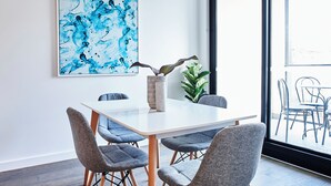 A modern dining area with a white table, grey upholstered chairs, and a large abstract painting on the wall.