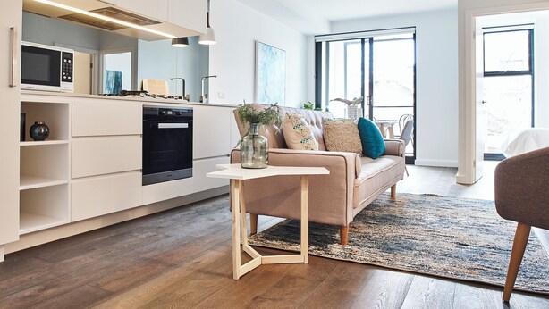 A modern kitchen with built-in appliances, a dining area with a sofa and a small table, and a large window providing natural light.
