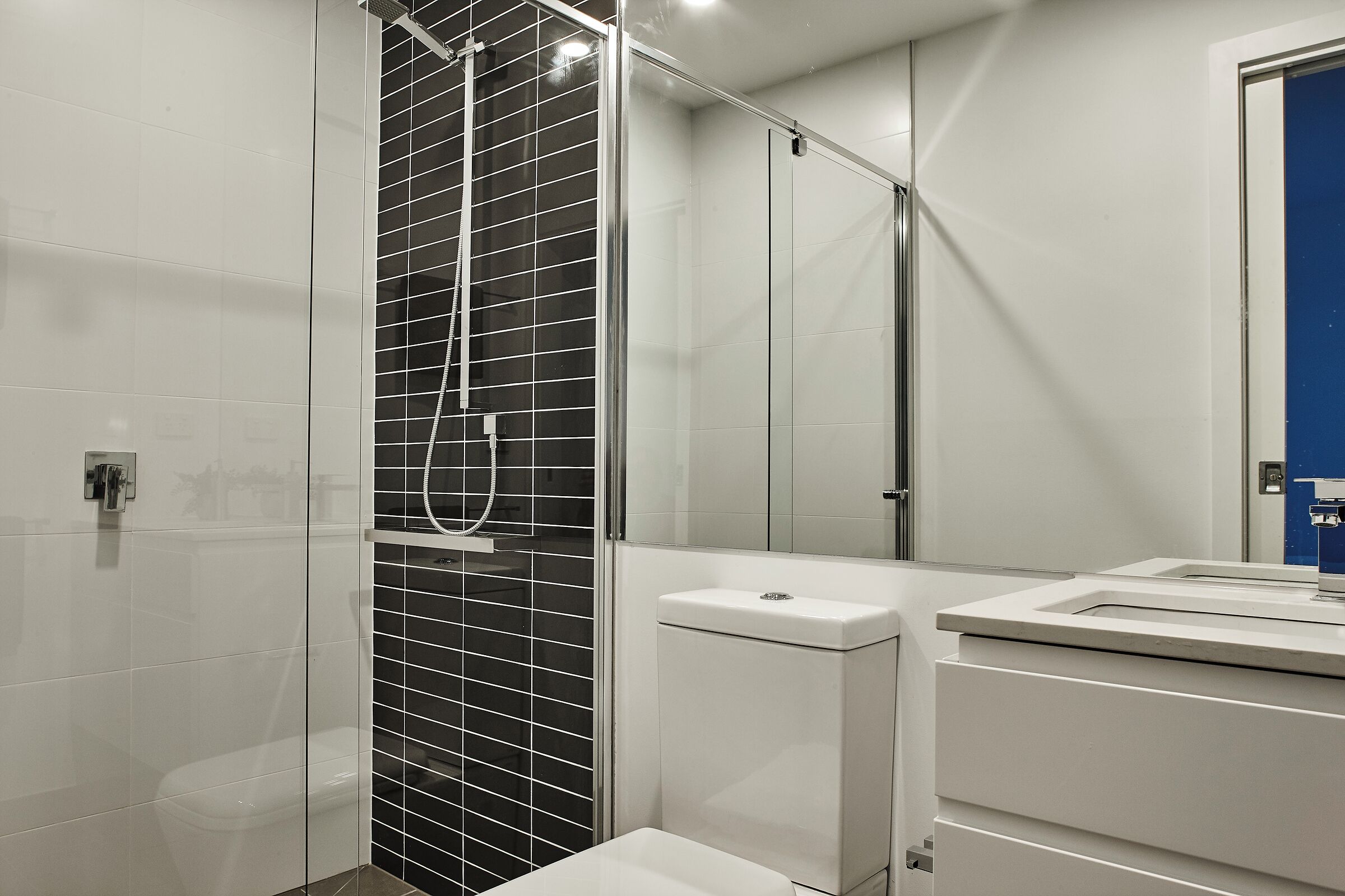 Une salle de bain moderne avec une douche à parois de verre, des toilettes blanches et un lavabo avec un miroir.