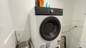 A compact laundry room with stacked washers and dryers, a small sink, and a drying rack.