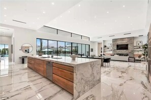 A modern kitchen with a marble countertop, wooden cabinets, and a large island. - Sleeps 28 | 2 Luxe Villas w/ Pickleball Court | Bravo Villas Dorada by AvantStay (Indio)
