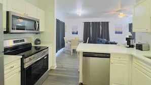 Cocina moderna con armarios blancos, microondas integrado, estufa y lavavajillas. Hay un comedor con mesa y sillas.