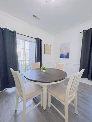 A dining room with a round table, four chairs, a potted plant, and artwork on the walls.