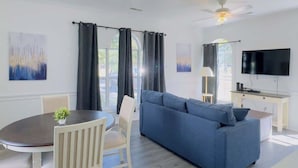 Una sala de estar moderna con un sofá azul, una mesa de comedor con sillas, un televisor de pantalla plana y un ventilador de techo.