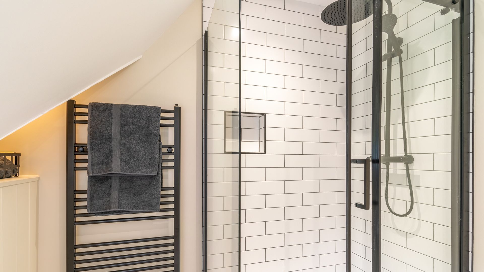 Un bagno moderno con piastrelle bianche a metro, cabina doccia in vetro e portasciugamani con un asciugamano scuro.