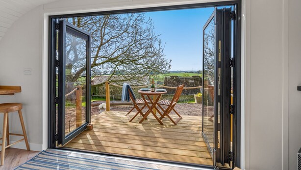 Ein modernes Zimmer mit einer Schiebetür zu einer Terrassenanlage mit Holztisch und -stühlen, einer Taue und Blick ins Grüne.