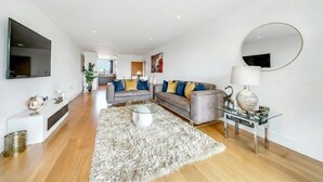 A modern living room with a grey sofa, a glass coffee table, and a round mirror on the wall.