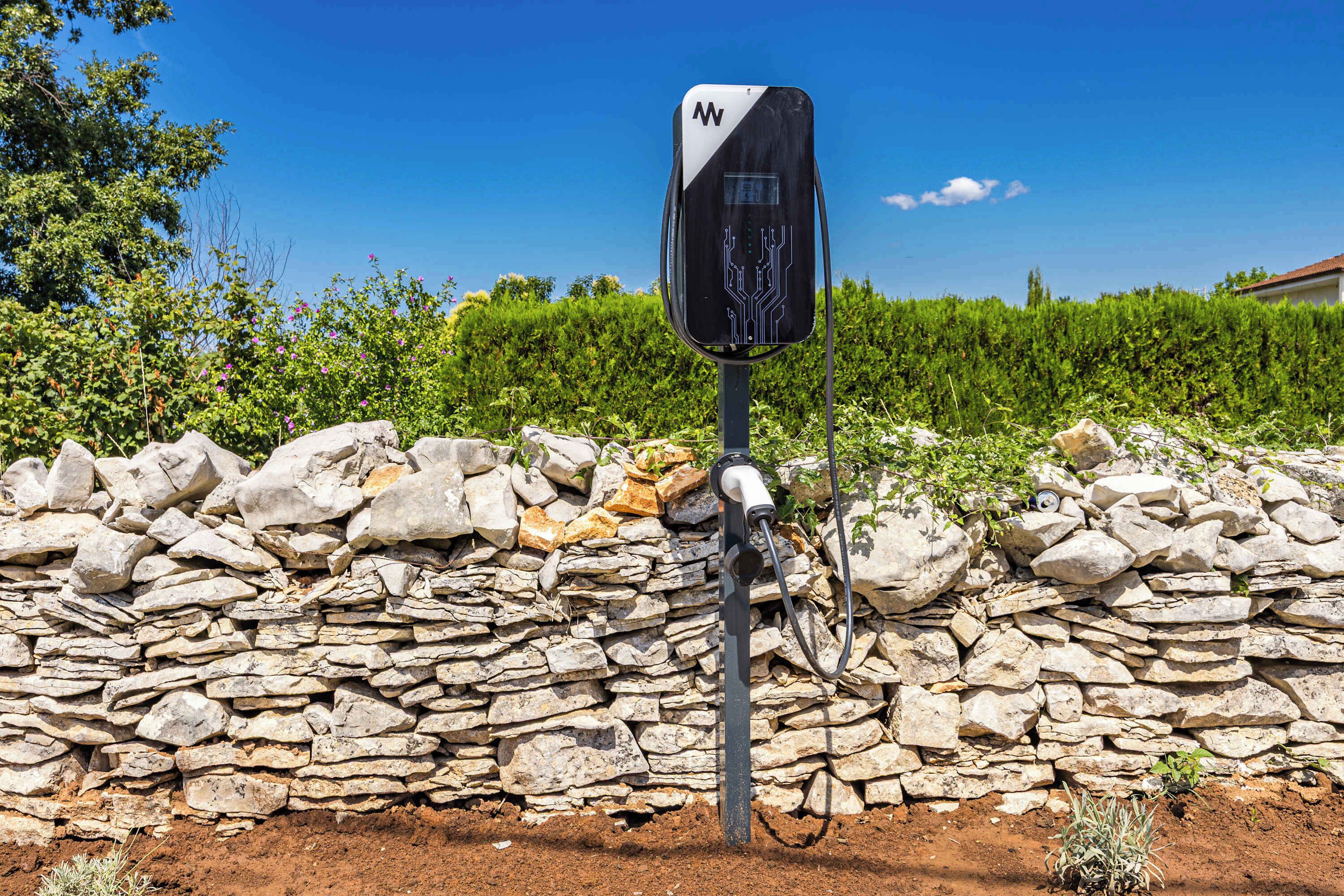 Un muro de piedra con un dispositivo electrónico negro sujeto a un poste.