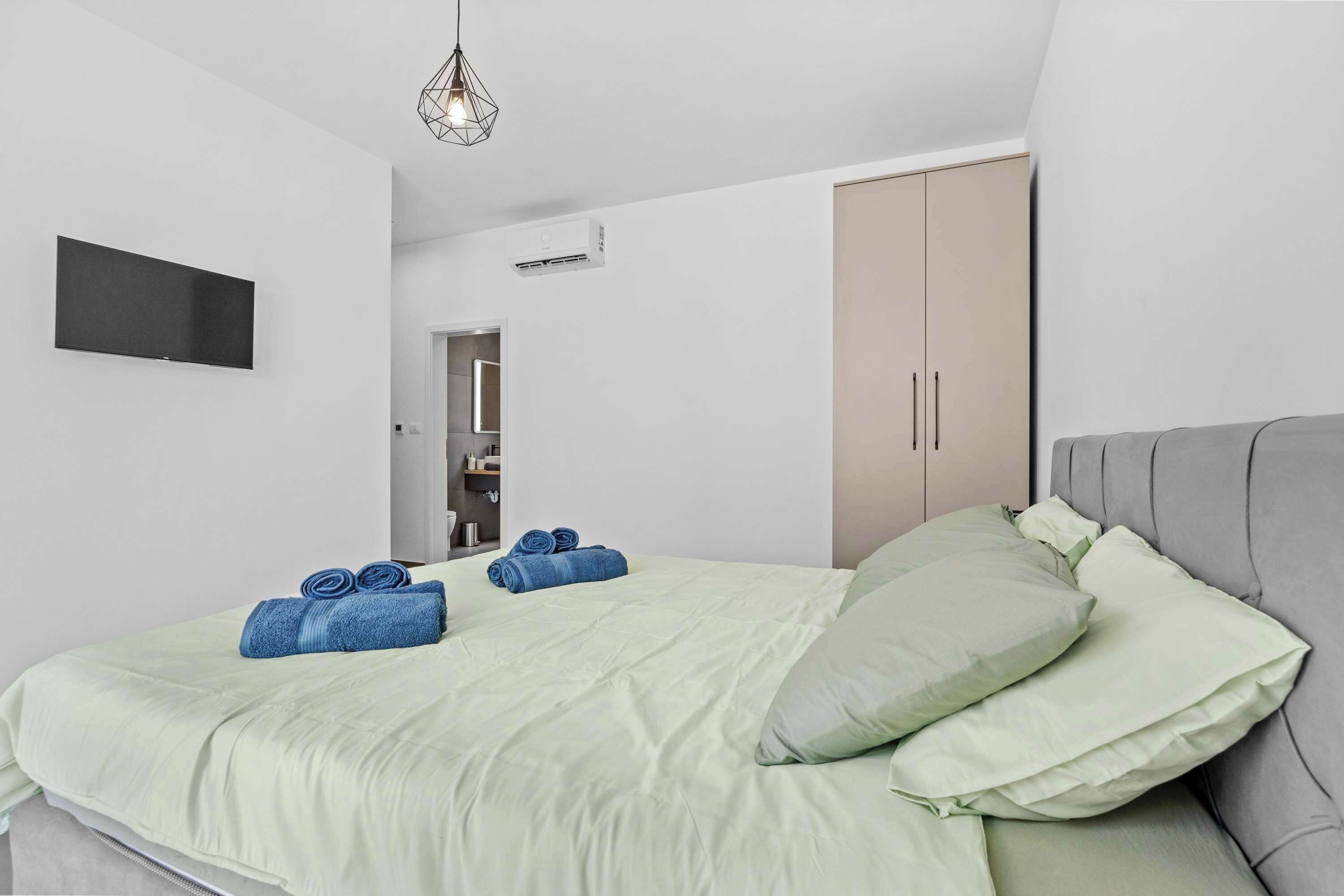 Une chambre à coucher moderne avec un lit, des oreillers, une télévision et une armoire.