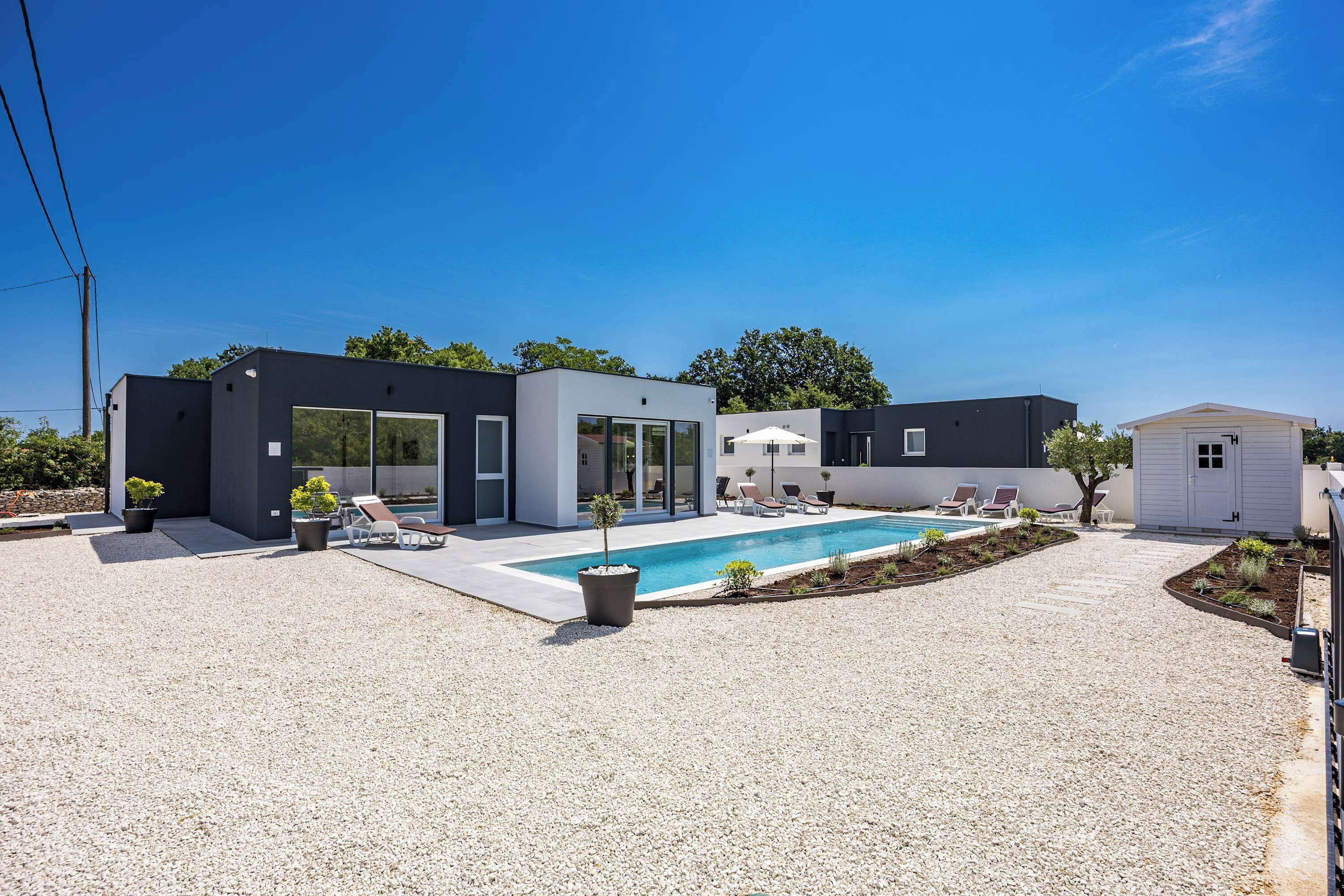 Una casa moderna con piscina, mobiliario de exterior y jardín.