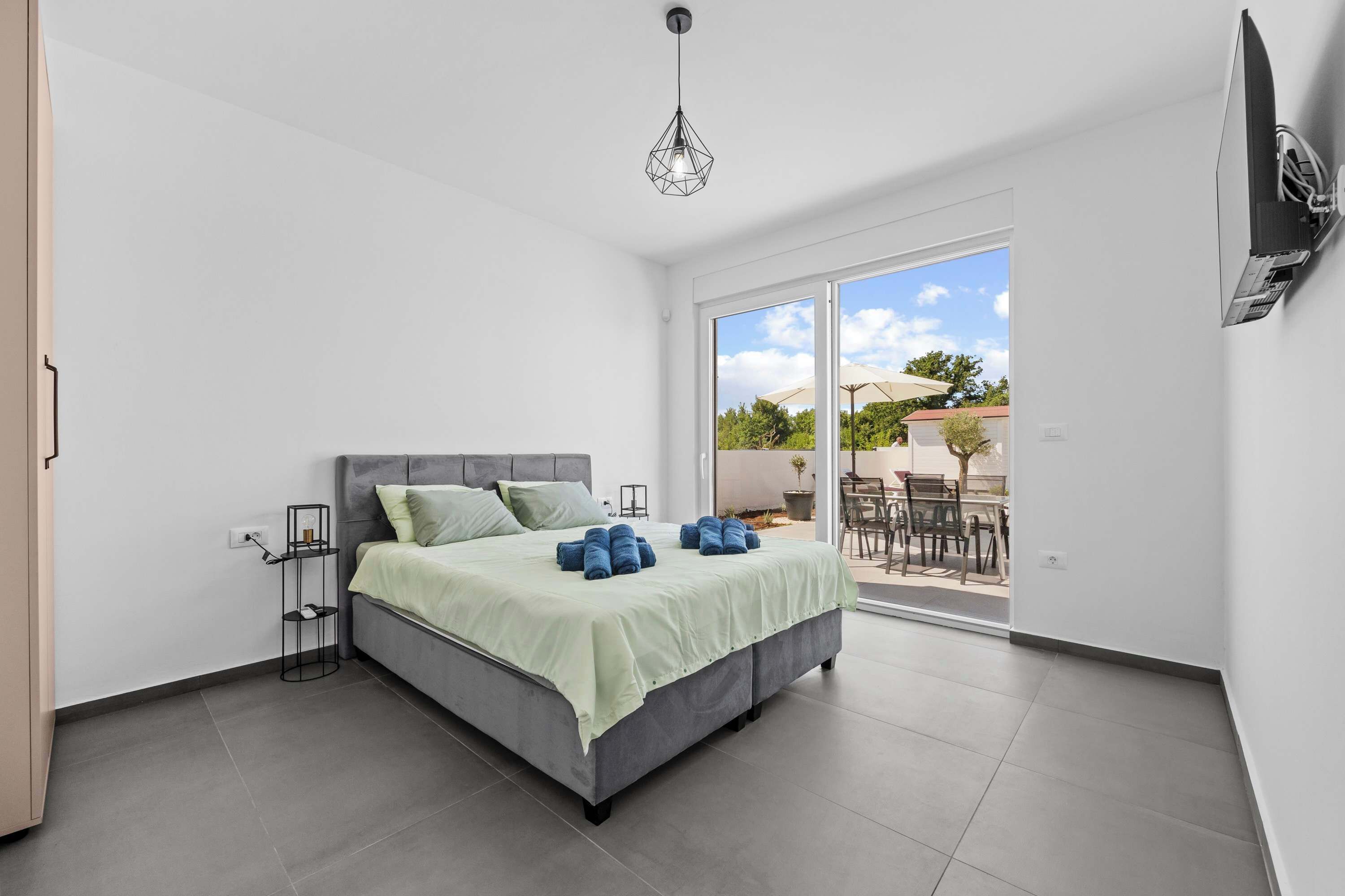 Camera da letto moderna con un letto, un comodino, una TV a parete e una porta scorrevole in vetro che dà su uno spazio esterno.