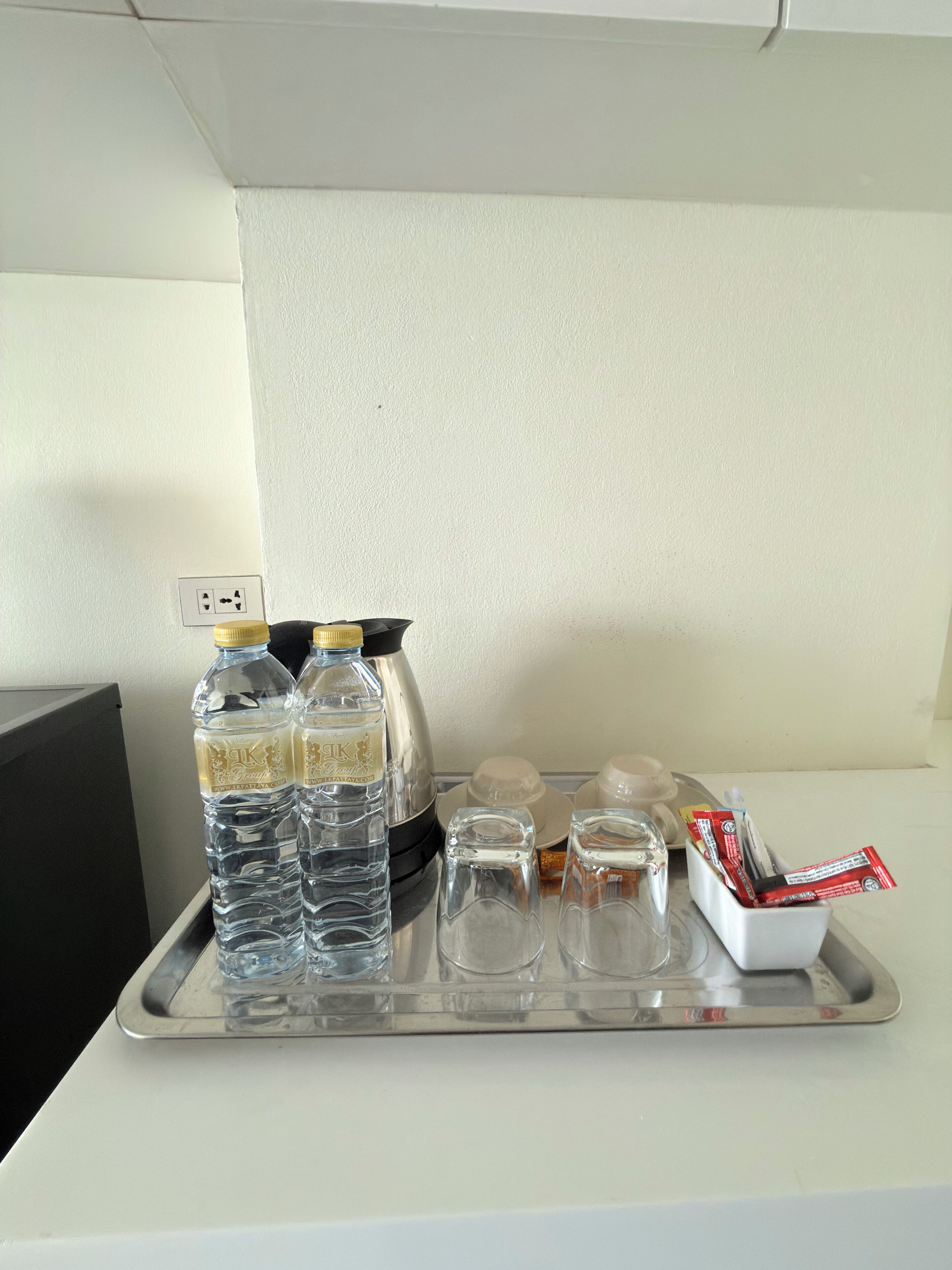 A tray with water bottles, a thermos, glasses, and a container of snacks on a hotel counter.
