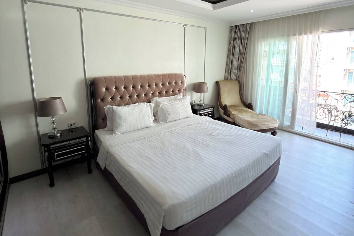A spacious bedroom with a large bed, a chair, a nightstand, and a window with a view.