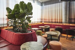 Un intérieur de restaurant moderne avec des sièges rouges, des tables rondes et une grande plante servant de pièce maîtresse décorative.