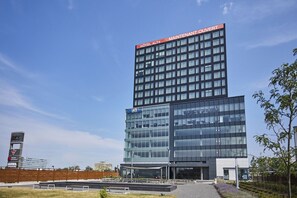 Un hôtel moderne, avec une enseigne bien visible indiquant : « HÔTEL ALT+ MAINTENANT OUVERT ».