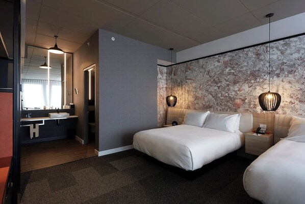 A modern hotel room with a large bed, a separate bathroom with a vanity, and a patterned wall.