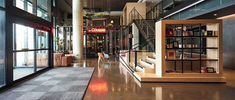 Un interior moderno con una escalera central, un área de descanso con sofás y una exhibición de objetos en estantes.