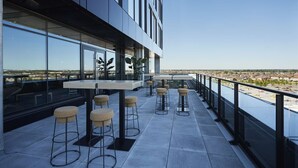 Eine Dachterrasse mit Barbereich, Sitzgelegenheiten und Blick auf die Stadtlandschaft.